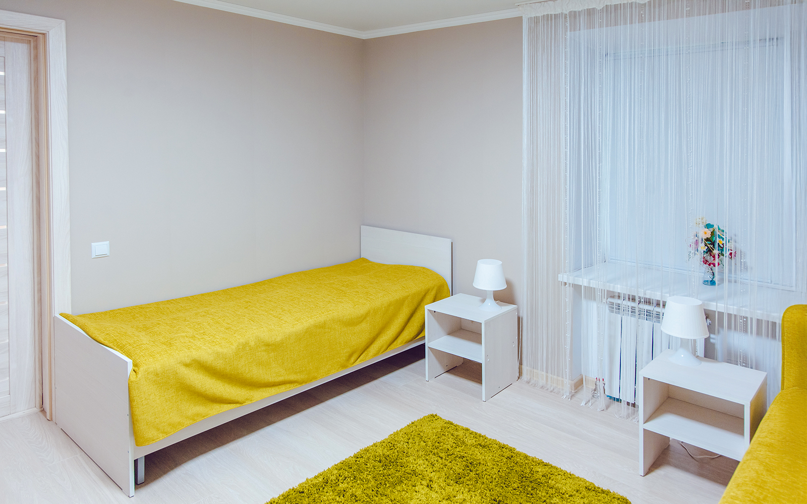 Hostel room with twin beds and window view of lush greenery.