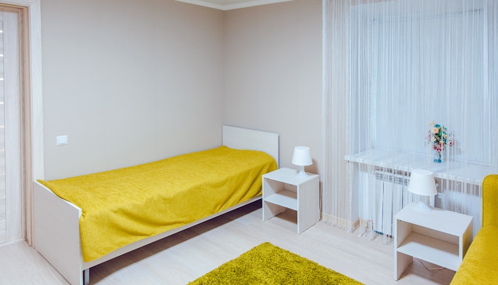 Hostel room with twin beds and window view of lush greenery.