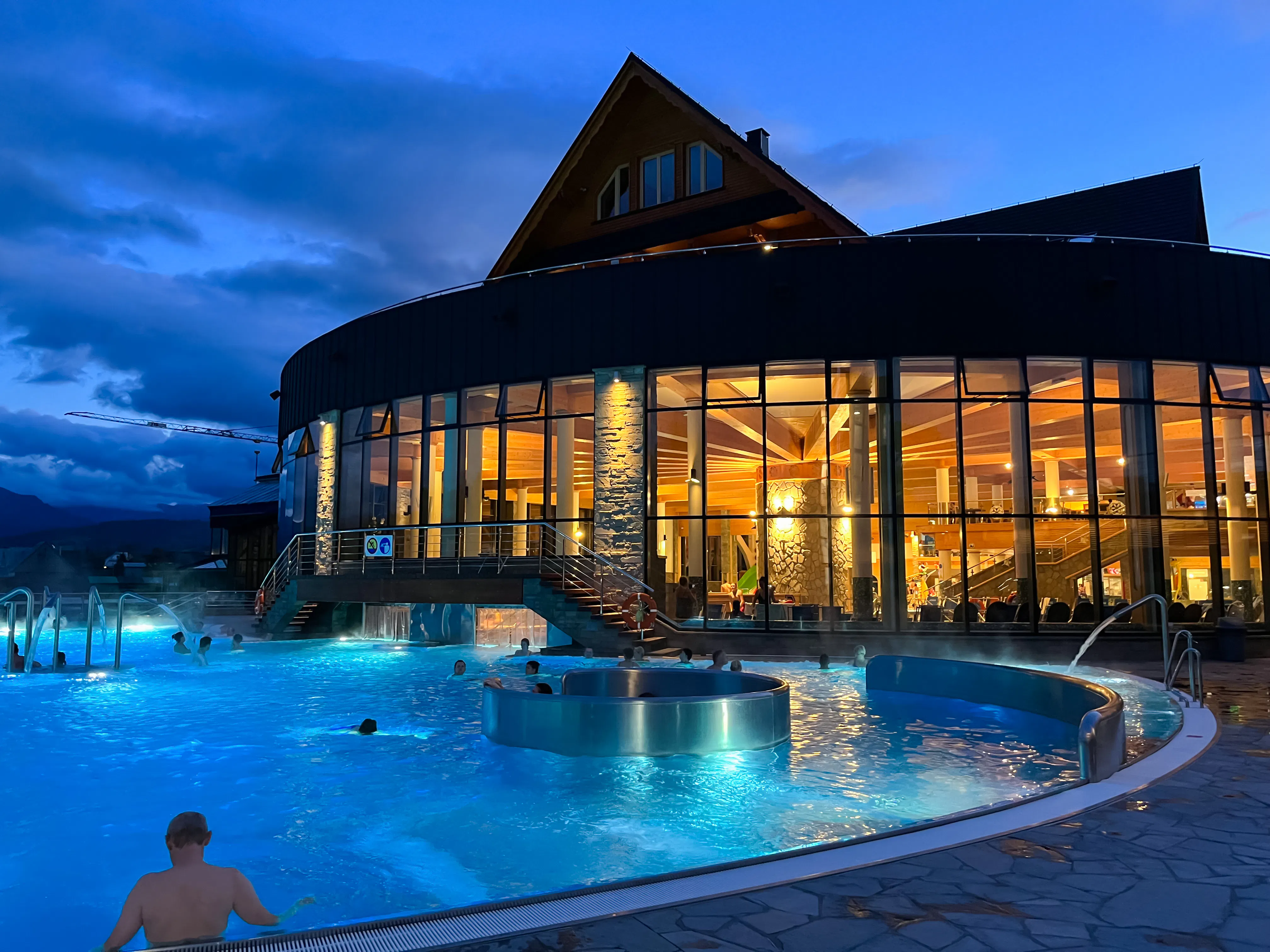 Thermal baths at night in Zakopane with illuminated building and Tatra Mountains backdrop.