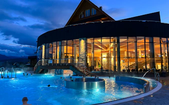 Thermal baths at night in Zakopane with illuminated building and Tatra Mountains backdrop.