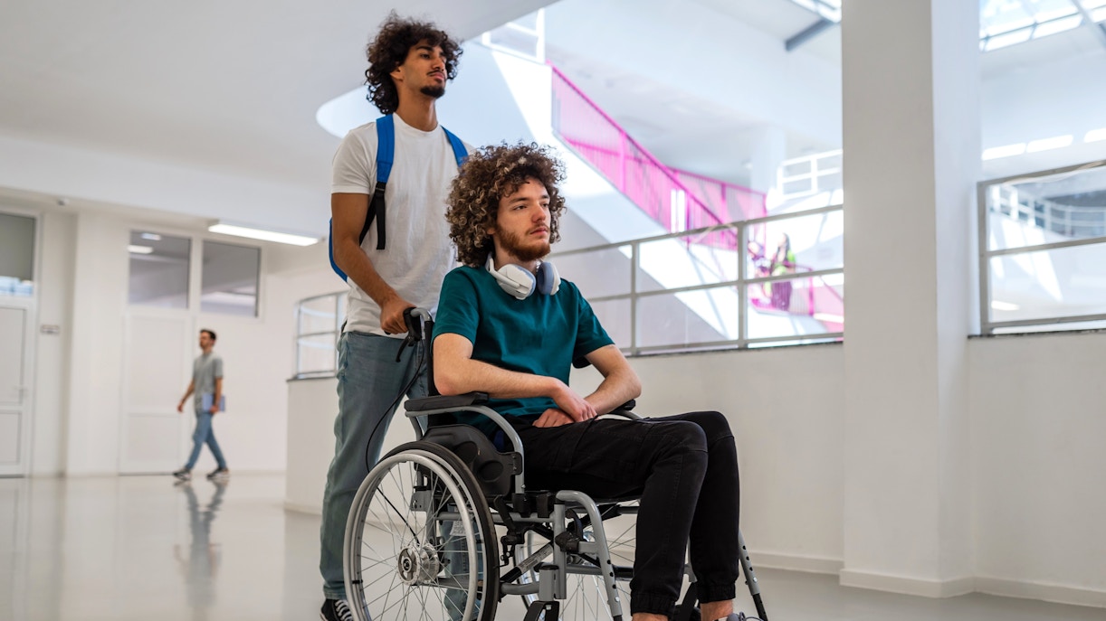 Person assisting another in a wheelchair through a bright, modern building.