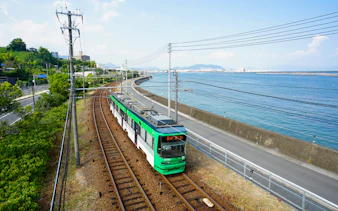 Tram traveling along the coast in Hiroshima, Japan, with ocean and cityscape views.