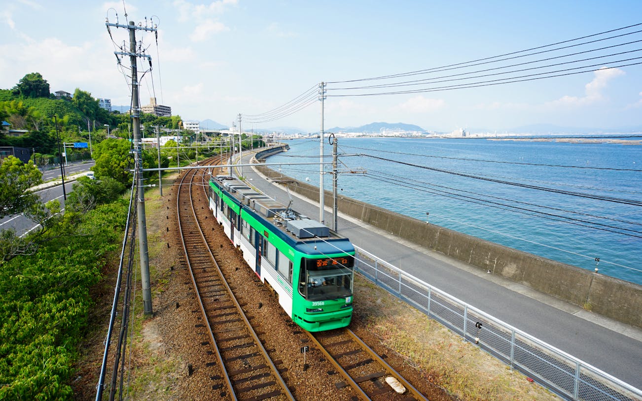Tram traveling along the coast in Hiroshima, Japan, with ocean and cityscape views.