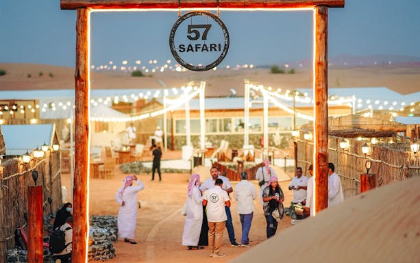 57 Heritage Desert Safari entrance with people gathering in a lit desert camp.