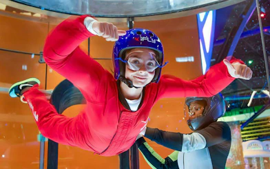 Person experiencing indoor skydiving at iFLY Quest with instructor guidance.