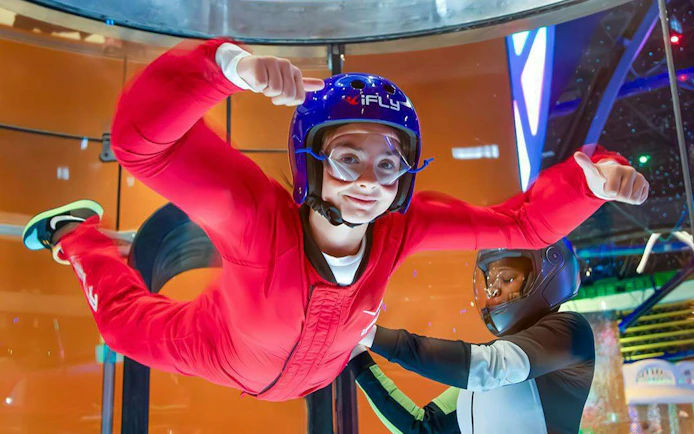 Person experiencing indoor skydiving at iFLY Quest with instructor guidance.