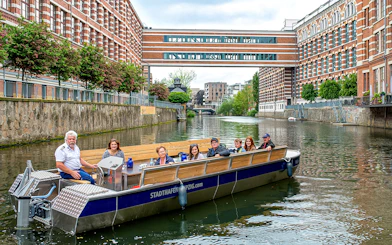 Guests on a motorboat tour of Karl Heine Canal, Leipzig, with historic buildings in view.