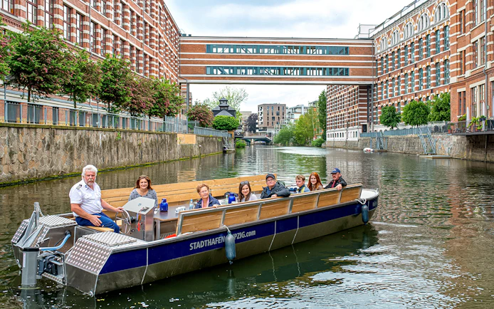 Guests on a motorboat tour of Karl Heine Canal, Leipzig, with historic buildings in view.