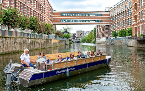 Guests on a motorboat tour of Karl Heine Canal, Leipzig, with historic buildings in view.