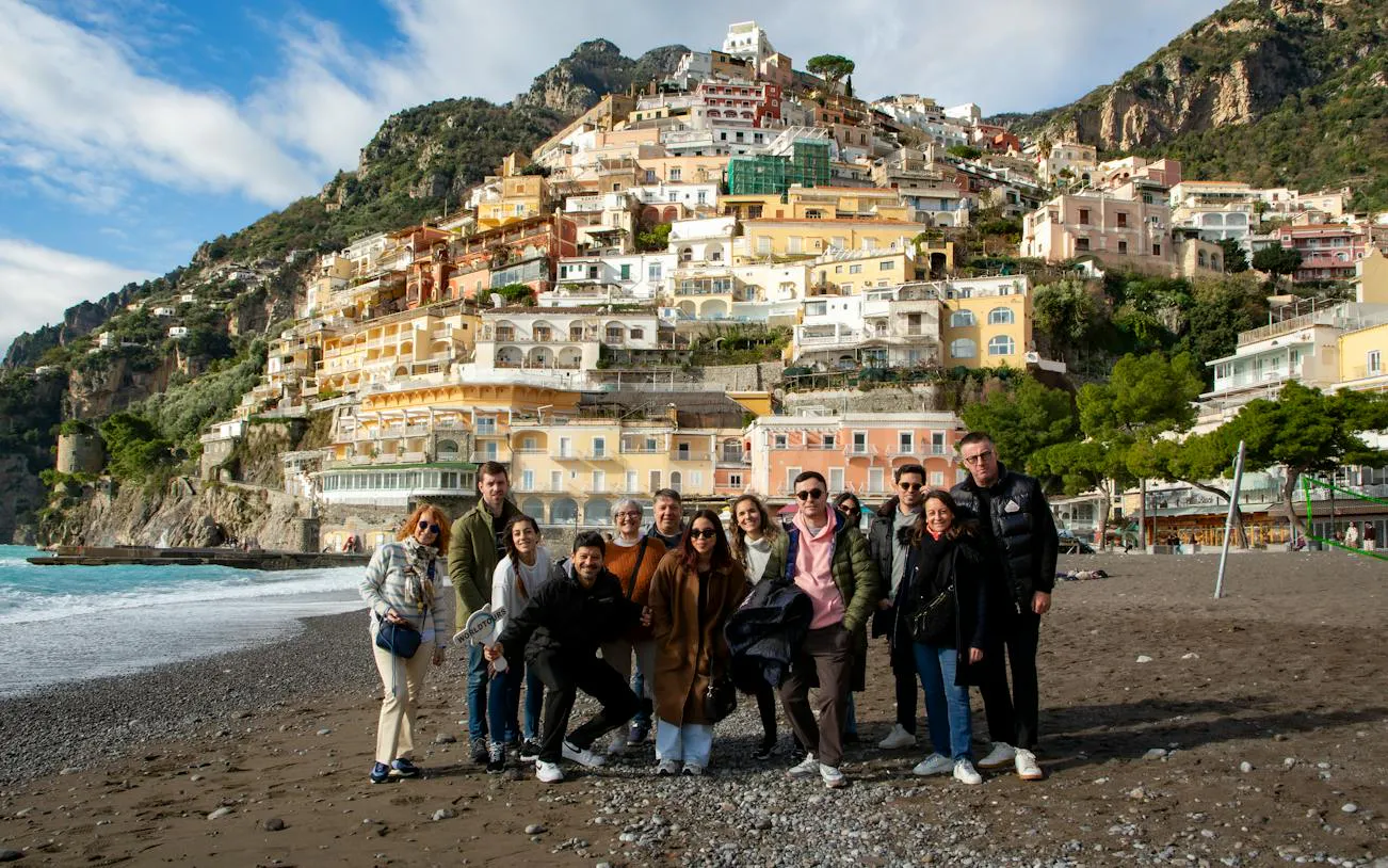 Group of tourists on Positano beach with colorful hillside buildings in the background.