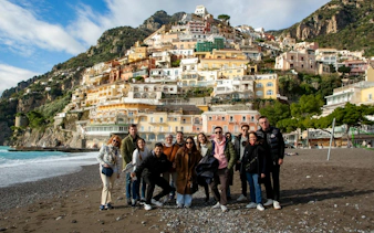 Group of tourists on Positano beach with colorful hillside buildings in the background.