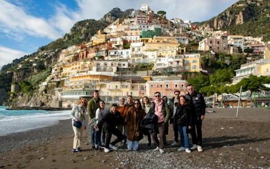 Group of tourists on Positano beach with colorful hillside buildings in the background.