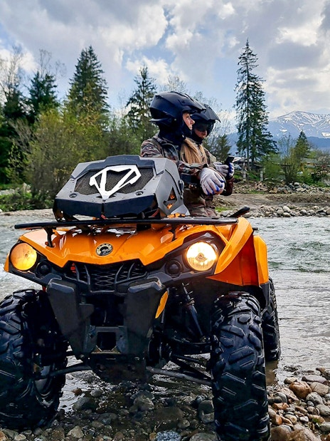 Visitors riding a quad bike by a river in Zakopane with mountains in the background.