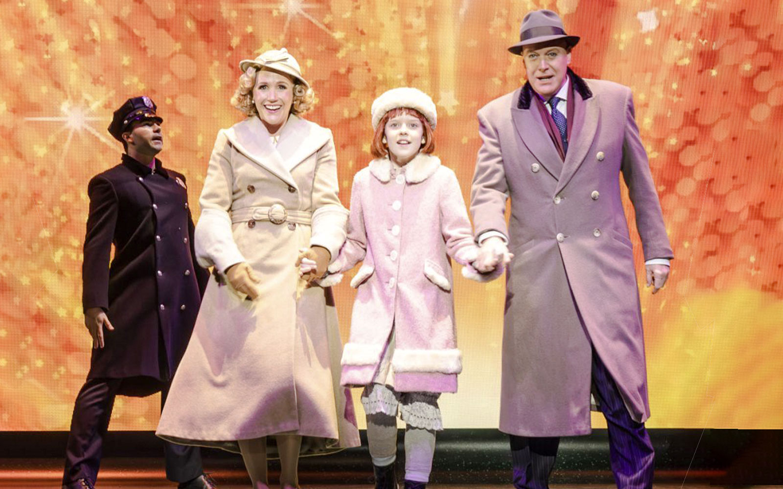 Performers in winter coats on stage during an Annie musical scene.