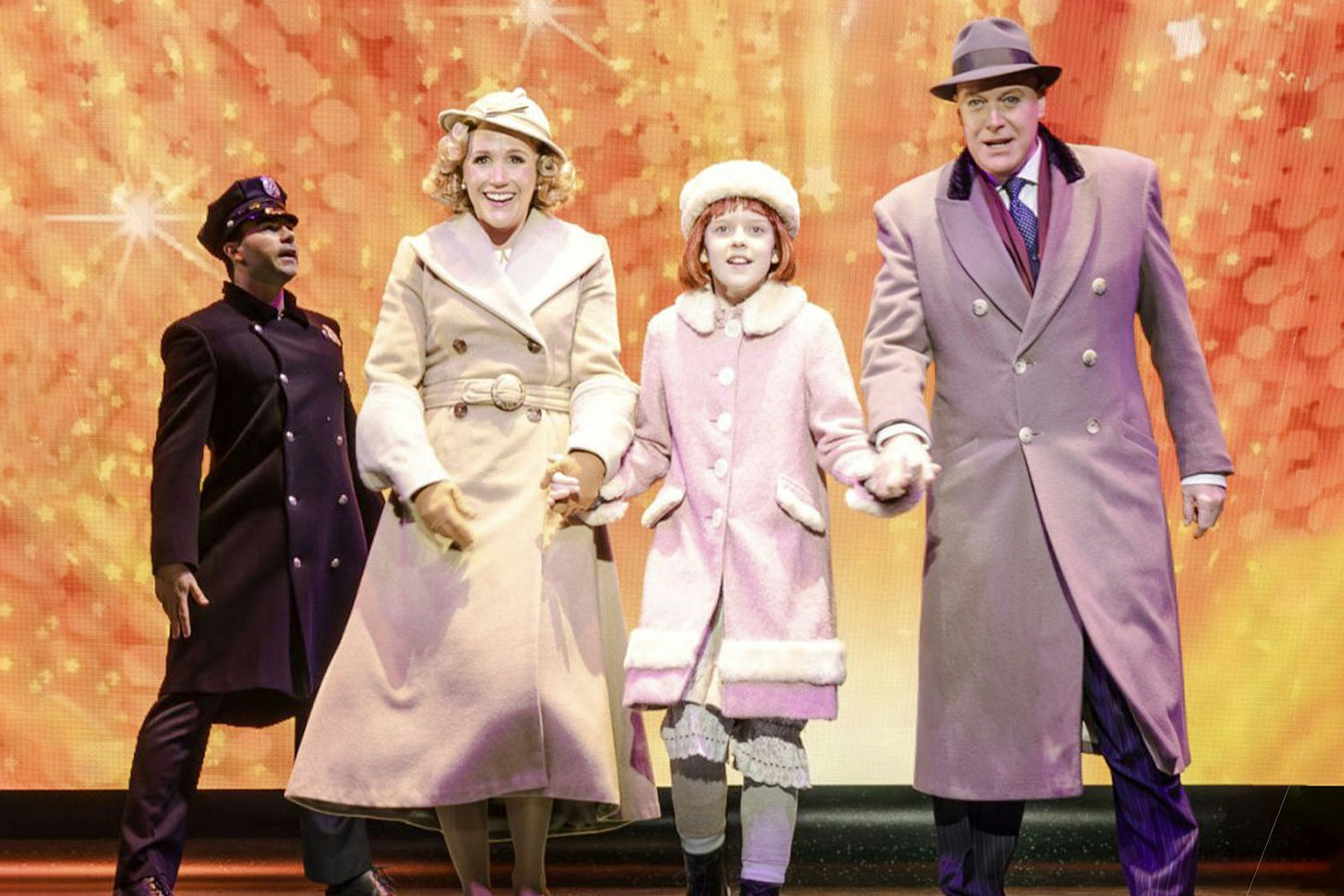 Performers in winter coats on stage during an Annie musical scene.