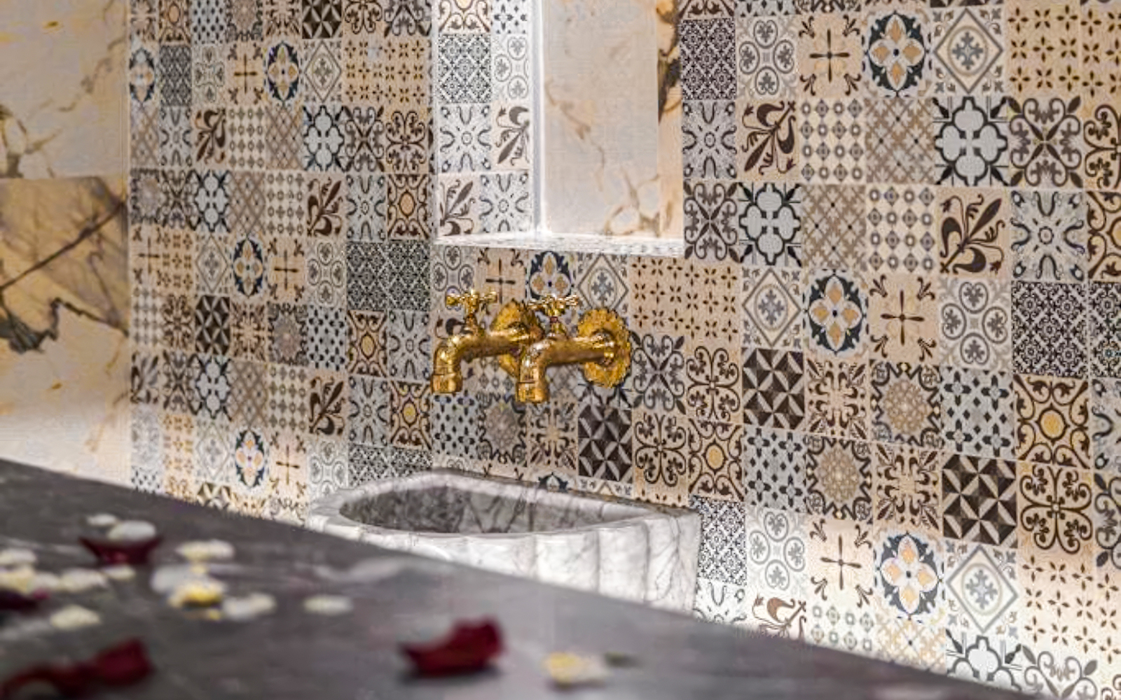 Ornate tile wall with golden faucets in a traditional hammam spa setting.