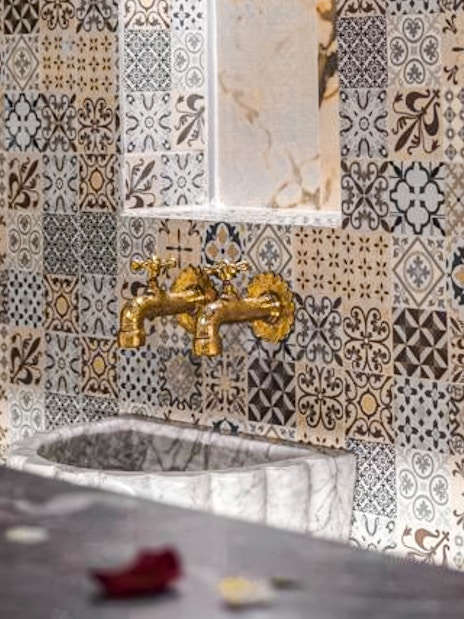 Ornate tile wall with golden faucets in a traditional hammam spa setting.