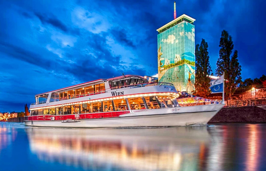 Danube River cruise boat at night with illuminated cityscape in Vienna.