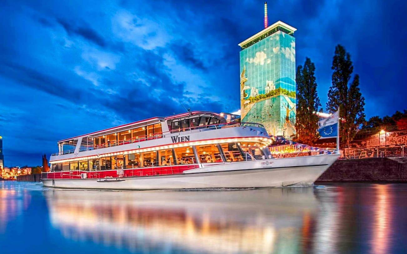 Danube River cruise boat at night with illuminated cityscape in Vienna.