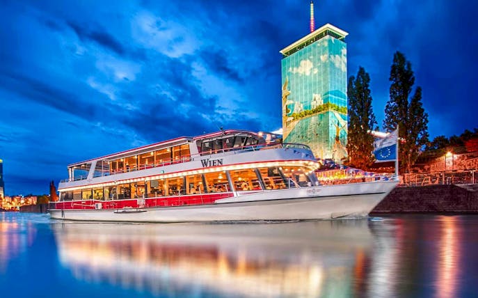 Danube River cruise boat at night with illuminated cityscape in Vienna.