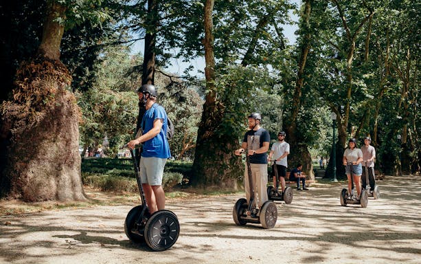 Tourists riding Segways with a guide in a tree-lined park during a guided tour in Porto.