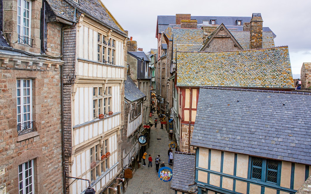 Narrow street in Mont Saint-Michel with historic stone and timber buildings, view from above.