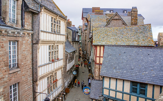 Narrow street in Mont Saint-Michel with historic stone and timber buildings, view from above.