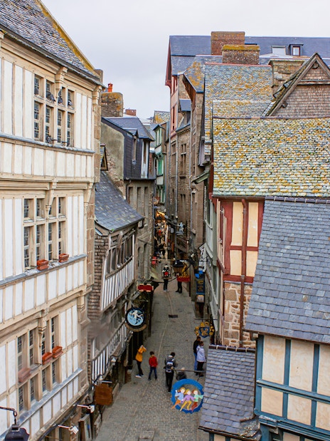 Narrow street in Mont Saint-Michel with historic stone and timber buildings, view from above.