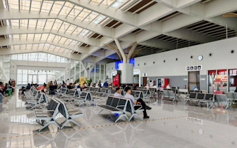 Passengers seated in Noi Bai Airport departure lounge, Hanoi, with visible signage and seating area.