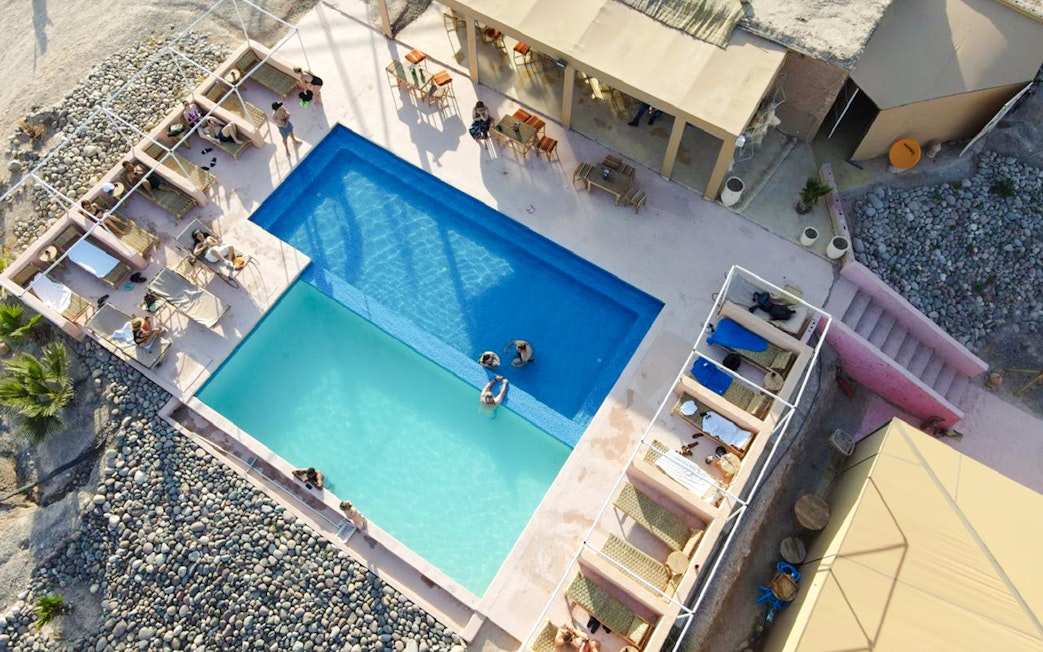 Aerial view of swimming pool at Marrakesh desert camp in Agafay, with sunbathers and loungers.