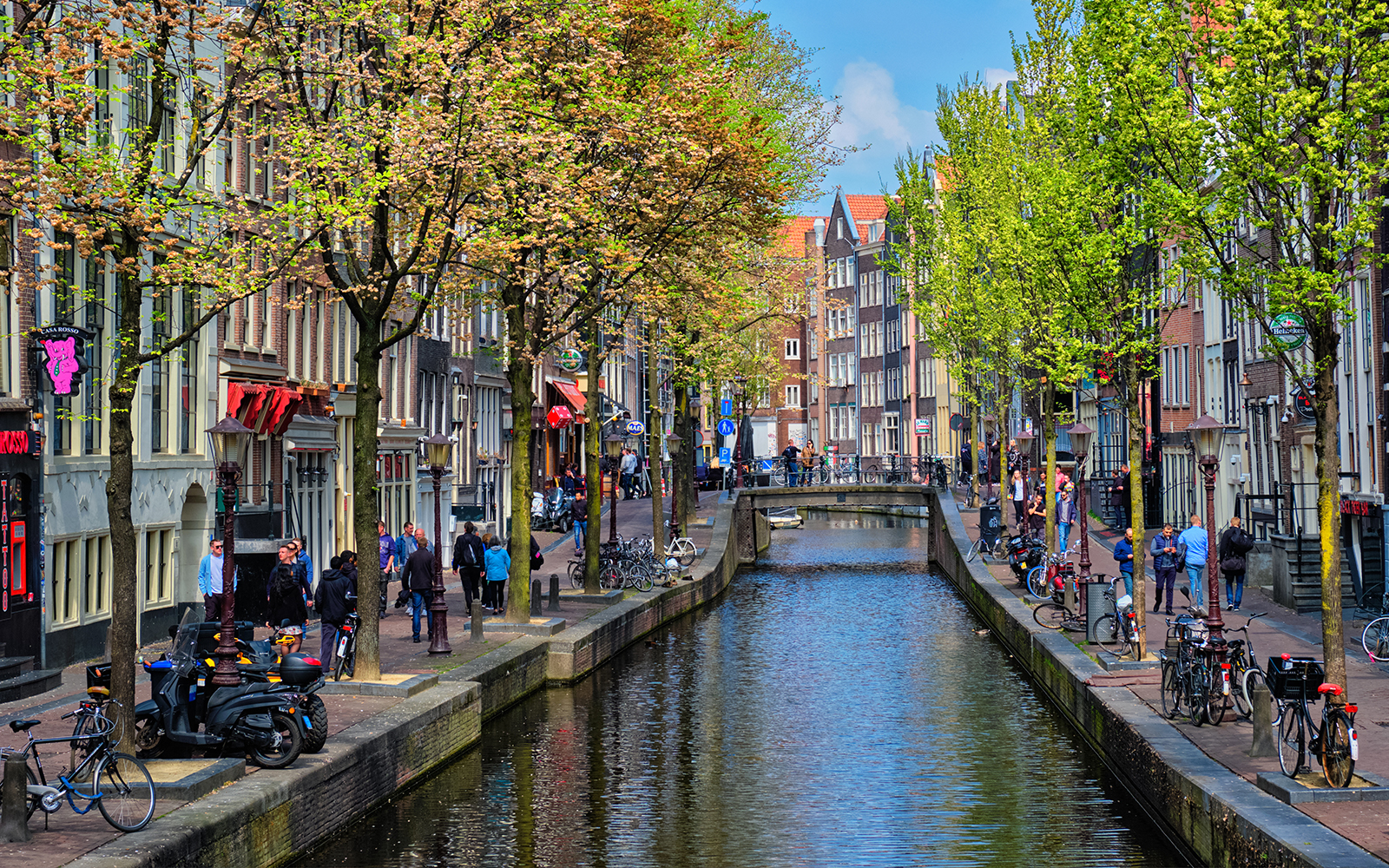 Canal view of Amsterdam's red light district during a cruise, with people walking along the canal.