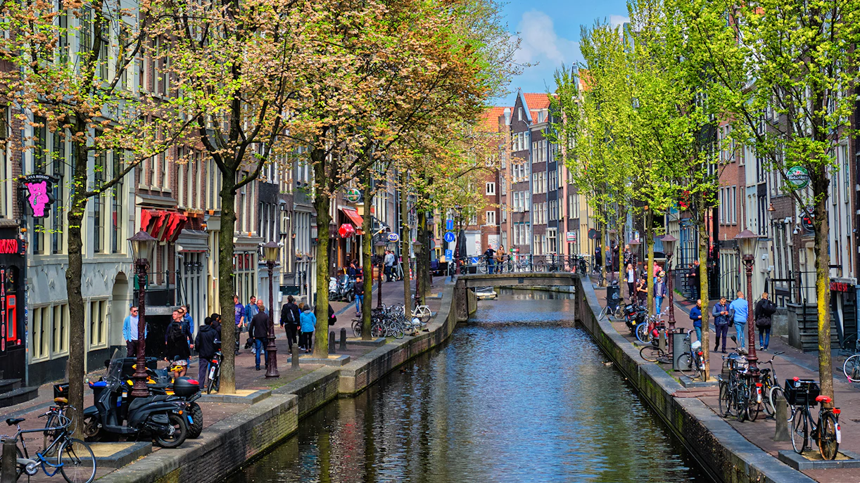 Canal view of Amsterdam's red light district during a cruise, with people walking along the canal.