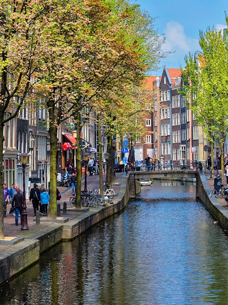 Canal view of Amsterdam's red light district during a cruise, with people walking along the canal.