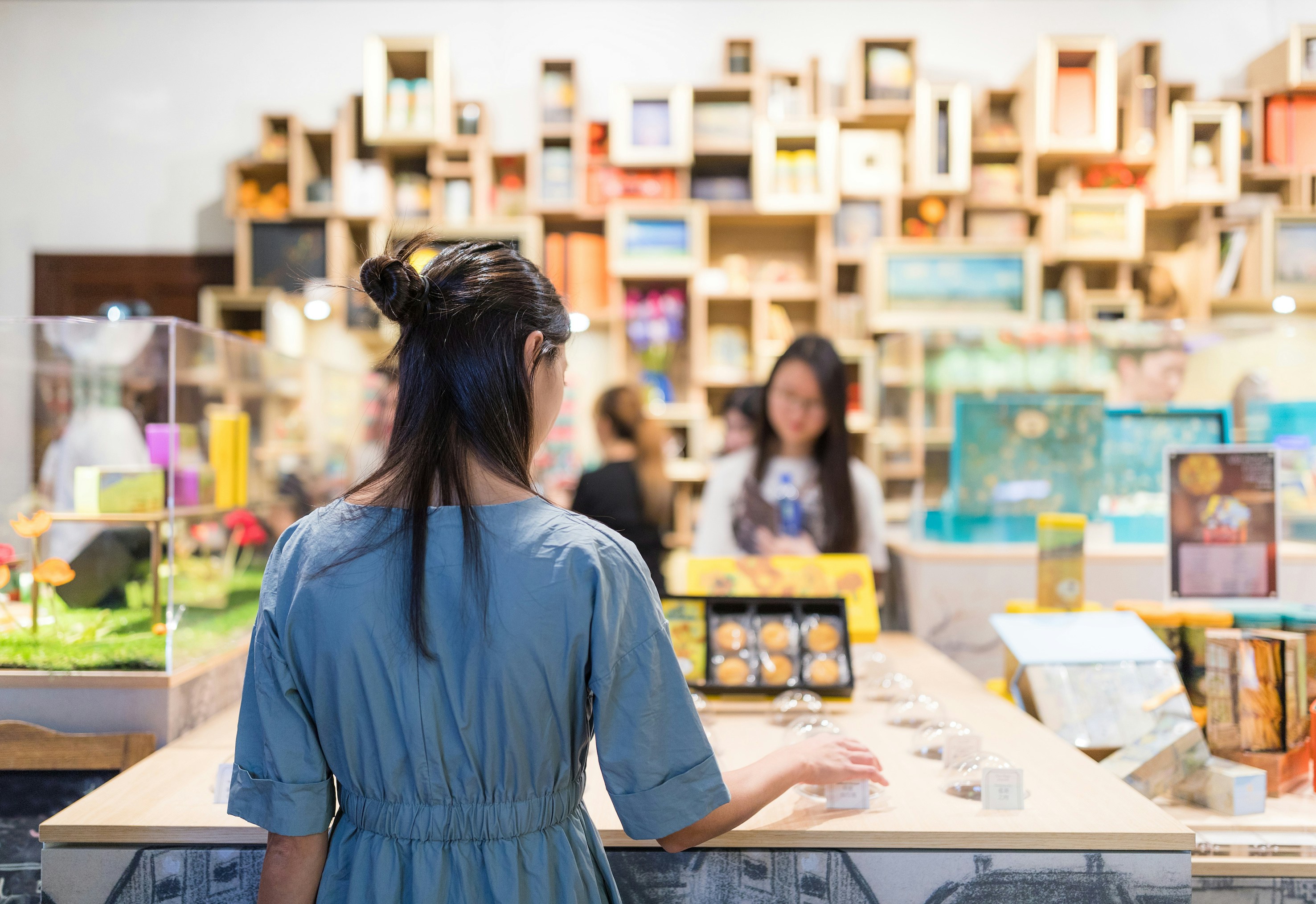 Woman browsing items in a gift shop with colorful shelves in the background.