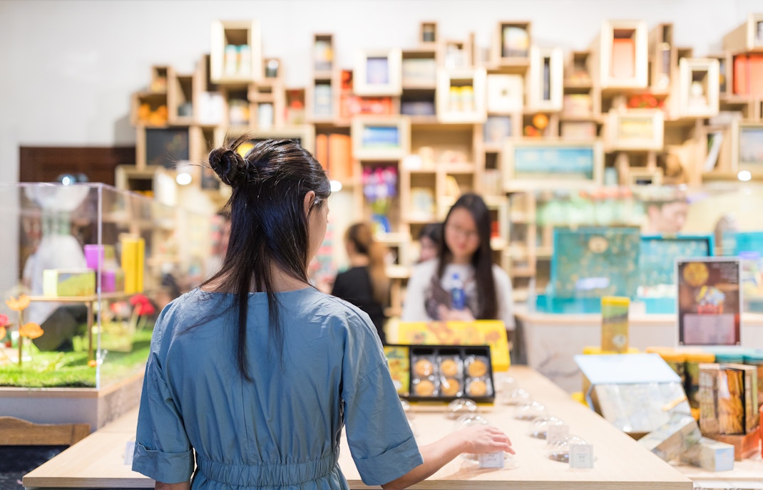 Woman browsing items in a gift shop with colorful shelves in the background.