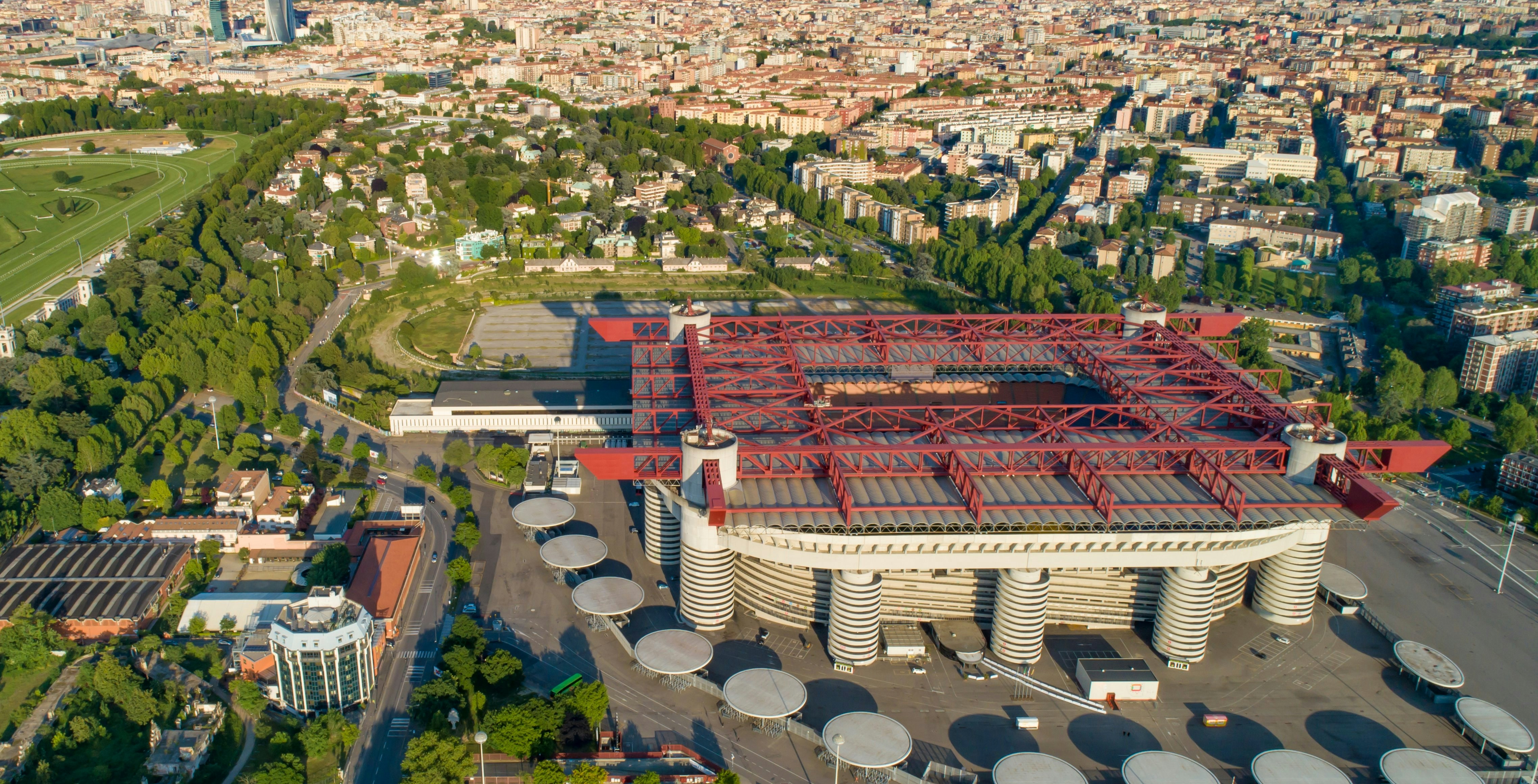 Aerial view of San Siro Stadium in Milan surrounded by cityscape and greenery.