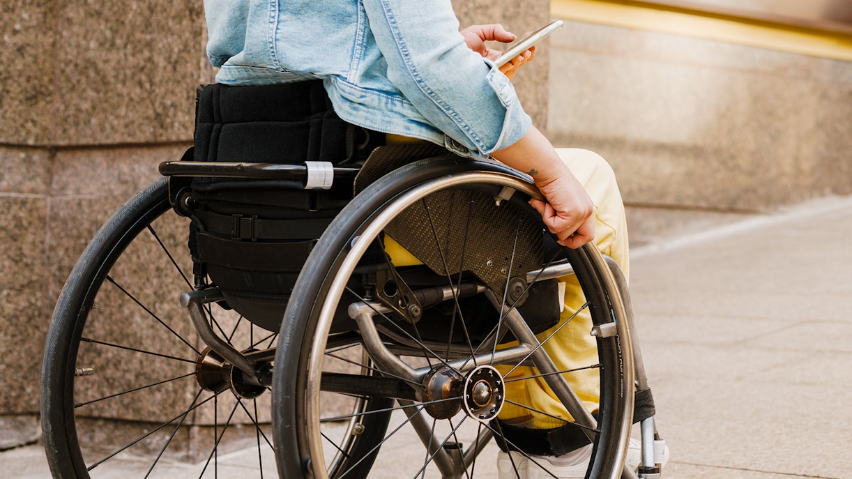 Girl in a wheelchair holding a smartphone on a city sidewalk.