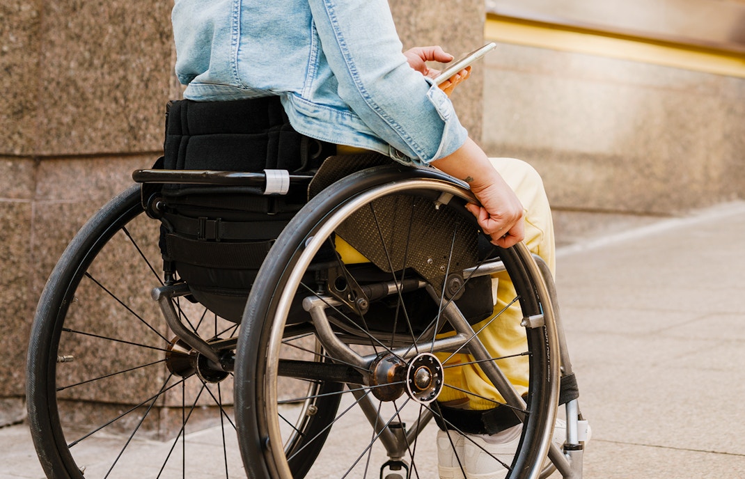 Girl in a wheelchair holding a smartphone on a city sidewalk.