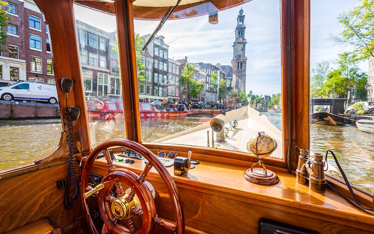 Steering wheel and interior view from a canal cruise boat in Amsterdam, with Westerkerk in the background.