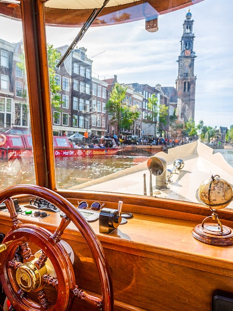 Steering wheel and interior view from a canal cruise boat in Amsterdam, with Westerkerk in the background.