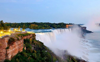 Niagara Falls USA at dusk with illuminated waterfalls and visitors on the observation deck.