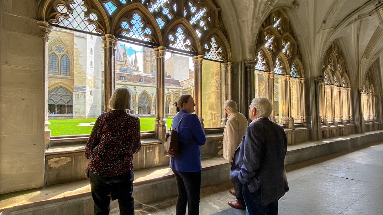 Tourists listening to a guide inside Westminster Abbey, viewing the cloisters.