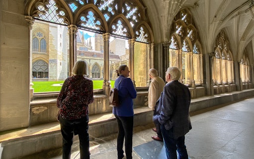 Tourists listening to a guide inside Westminster Abbey, viewing the cloisters.