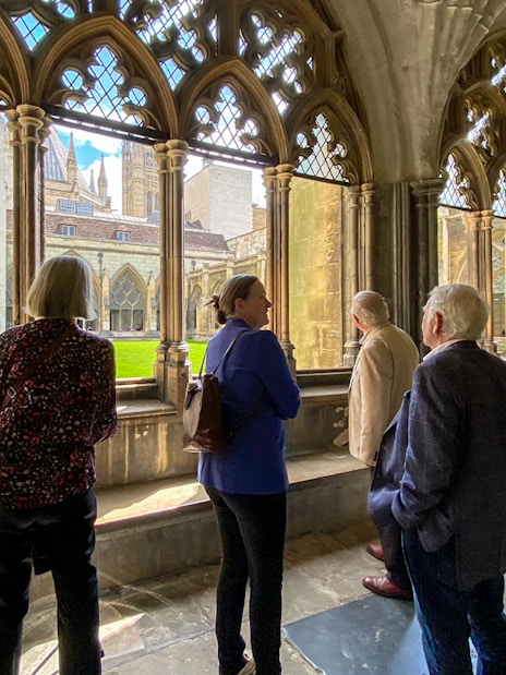 Tourists listening to a guide inside Westminster Abbey, viewing the cloisters.