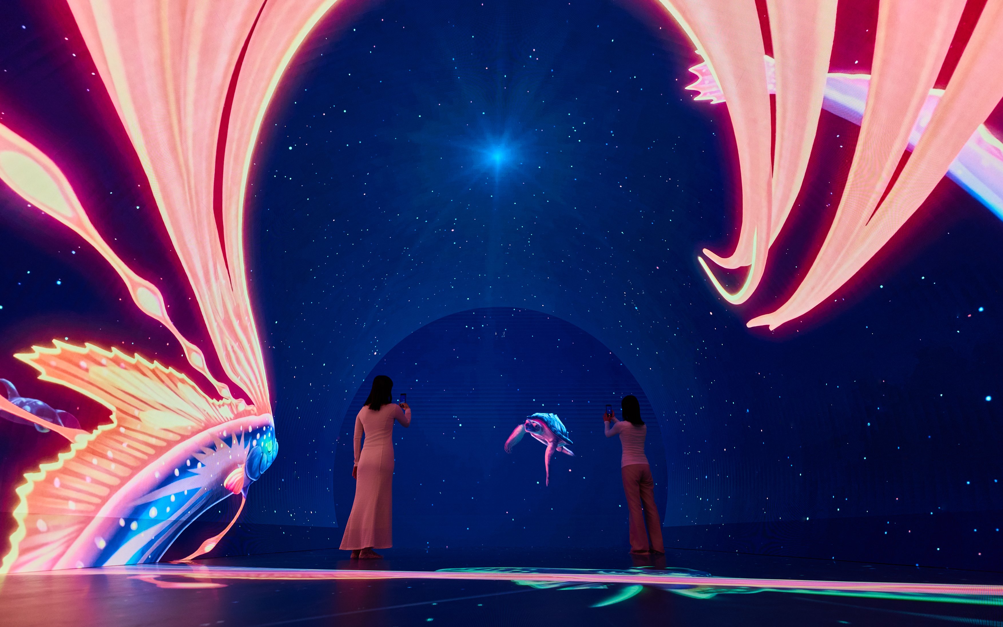 Visitors photographing digital art display at Wonderia YOKOHAMA, featuring vibrant marine life projections.