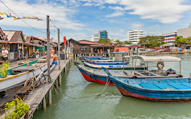 Boats docked at Clan Jetty in Penang, Malaysia, with stilt houses and visitors exploring.