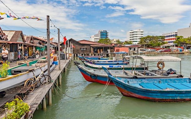 Boats docked at Clan Jetty in Penang, Malaysia, with stilt houses and visitors exploring.