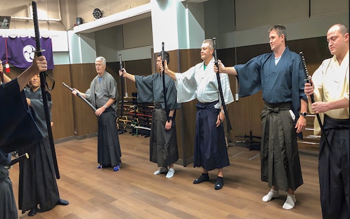Participants in traditional attire practicing sword techniques during a Samurai experience in Tokyo.