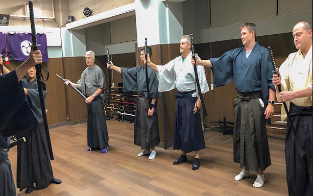 Participants in traditional attire practicing sword techniques during a Samurai experience in Tokyo.