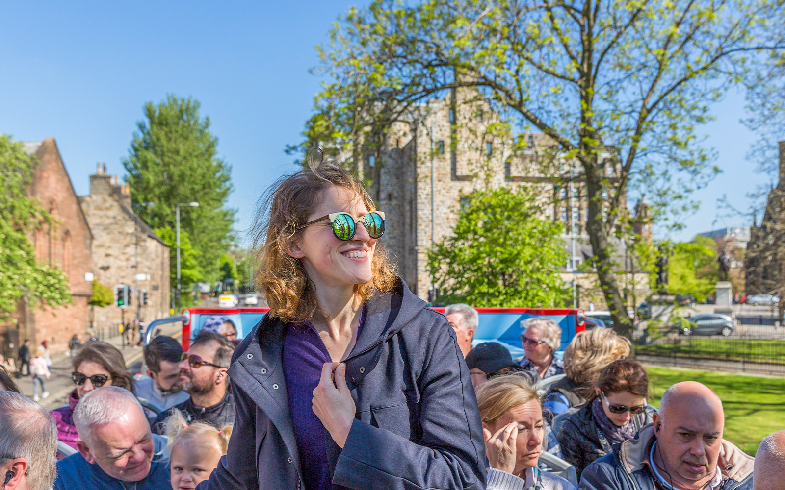 Tourists enjoying a sunny day on a hop-on hop-off bus tour in Glasgow.